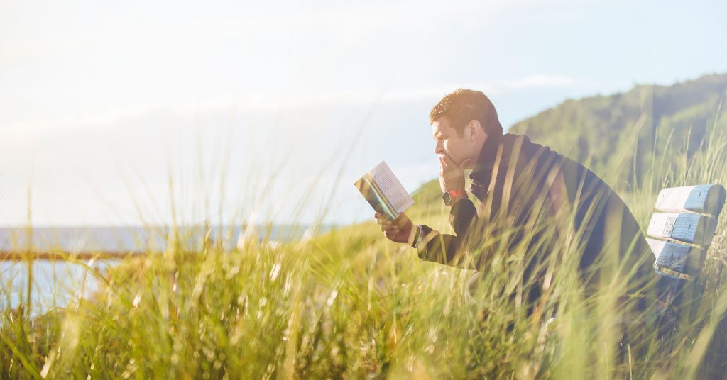 Man sitting in nature on a bench, while reading.