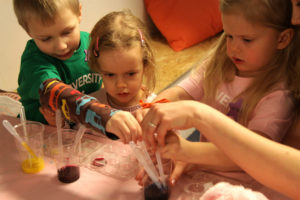 Kolme lasta harjoittelee pipettien käyttöä tiedekerhossa.