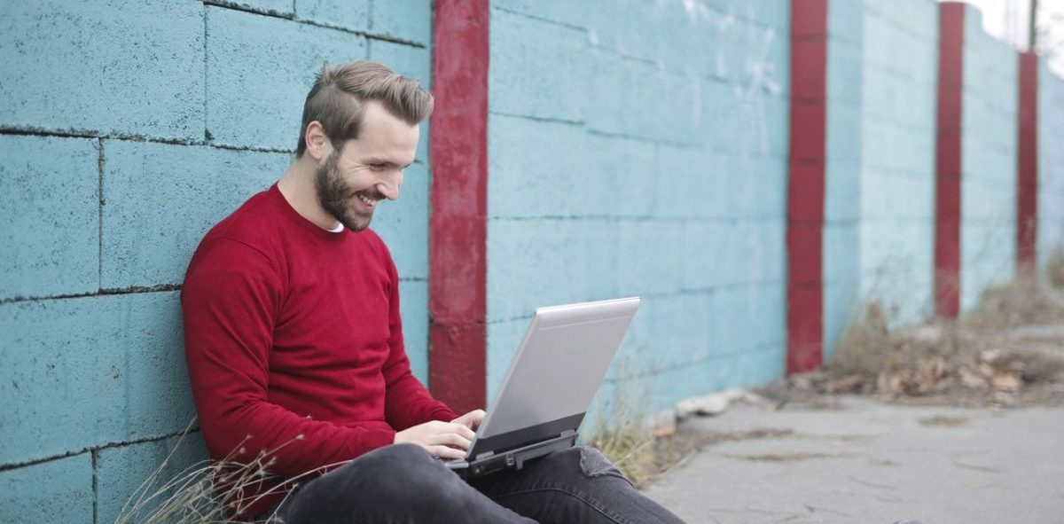 hymyilevä mies istuu ulkona tietokoneen äärellä