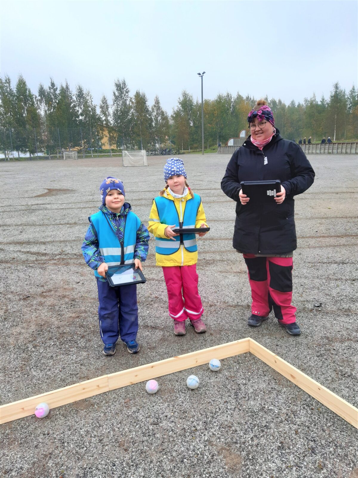 Opettaja ja kaksi lasta ohjelmoivat ulkona Sphero-robottipalloja.