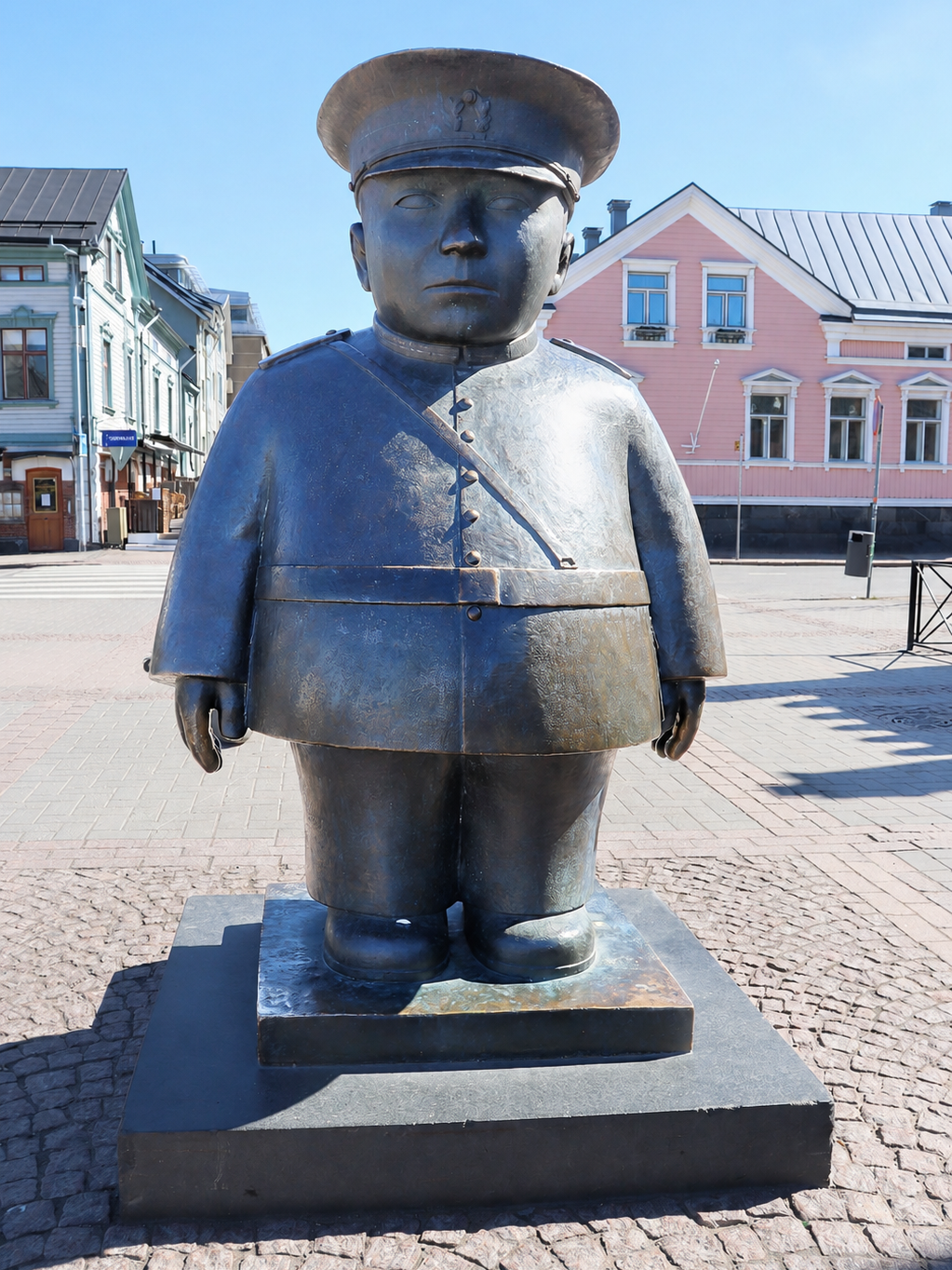 Oulun kauppatorilla oleva Toripolliisi-patsas, taustalla sininen ja vaaleanpunainen talo.