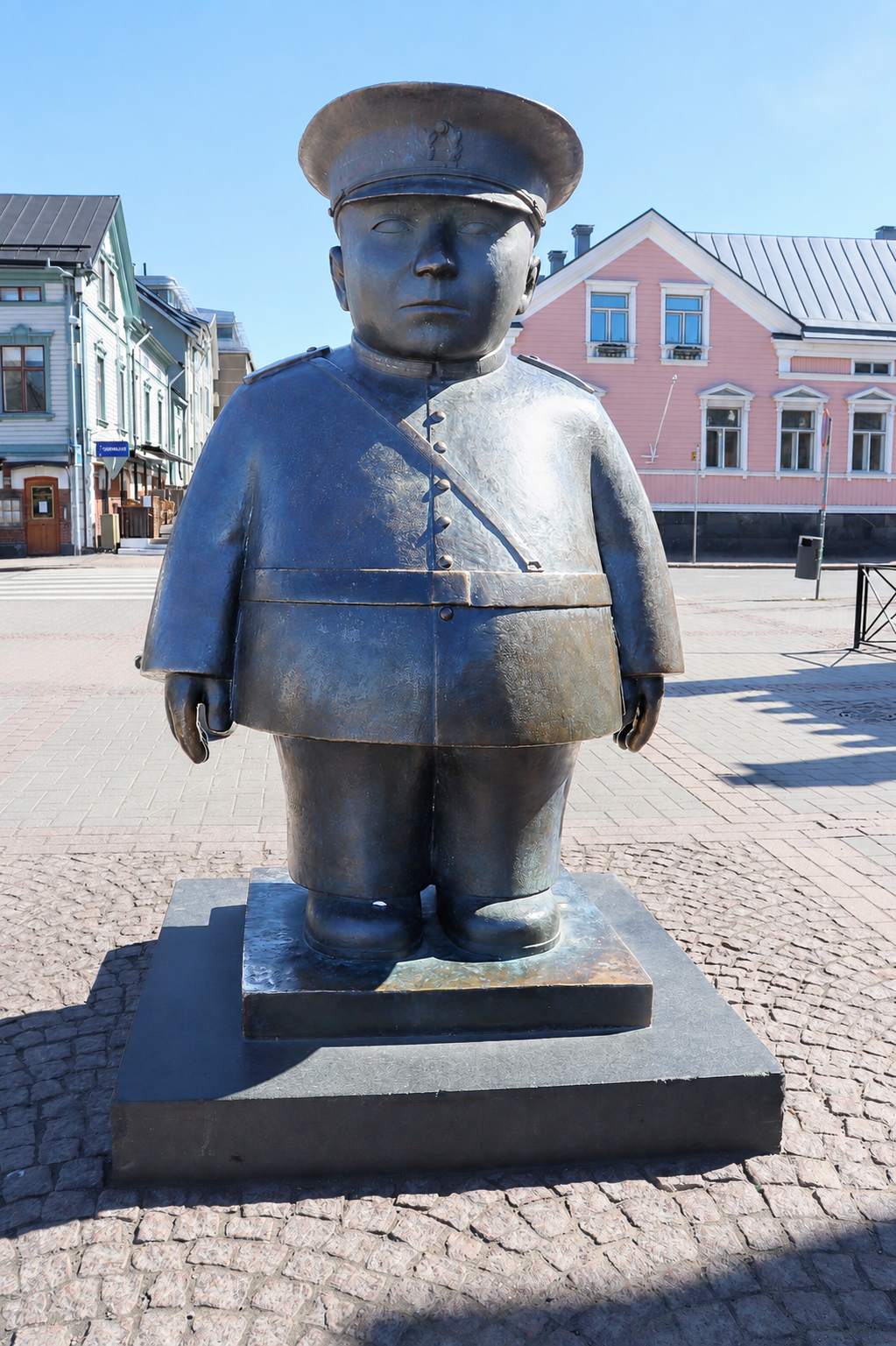 Oulun kauppatorilla oleva Toripolliisi-patsas, taustalla sininen ja vaaleanpunainen talo.